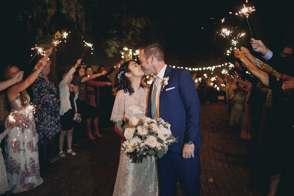 bride and groom kiss surrounded by guests holding sparklers