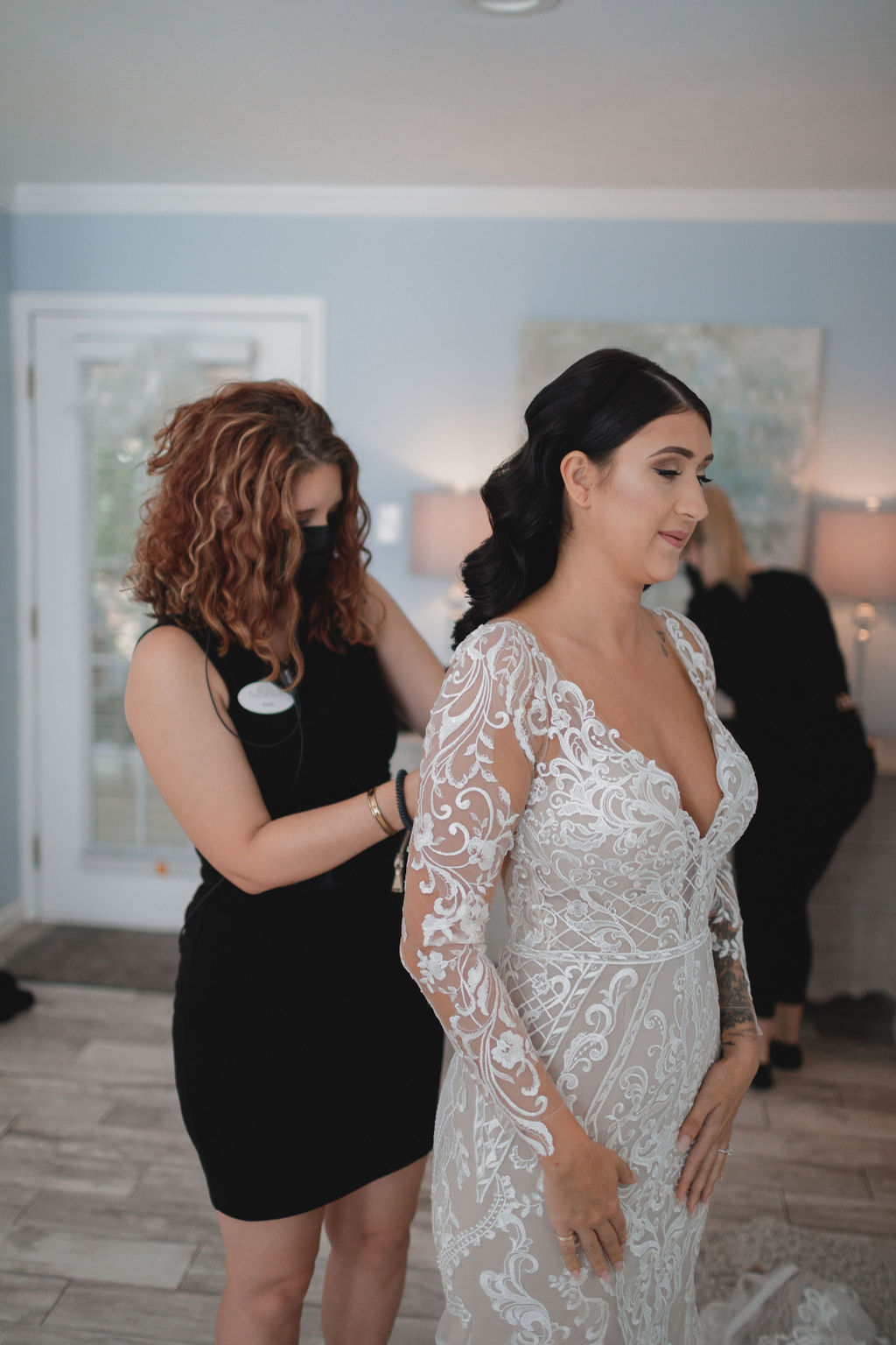 a wedding coordinator buttons a bride's dress
