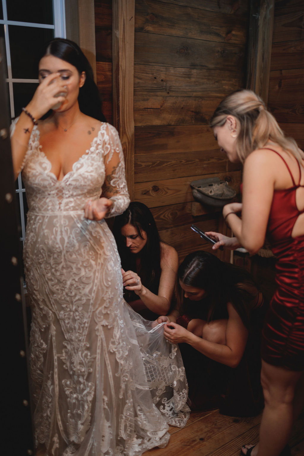 bridesmaids bustling a bride's dress while the bride takes a sip from a cup