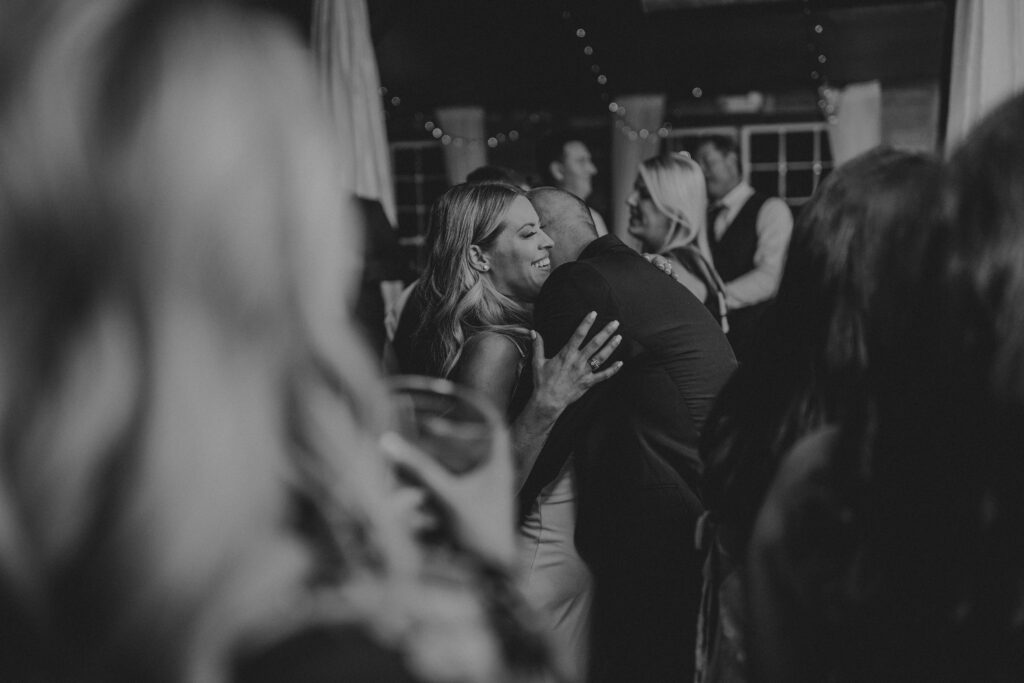 a black & white photo of a bride and groom embracing on a dancefloor in a crowd of guests