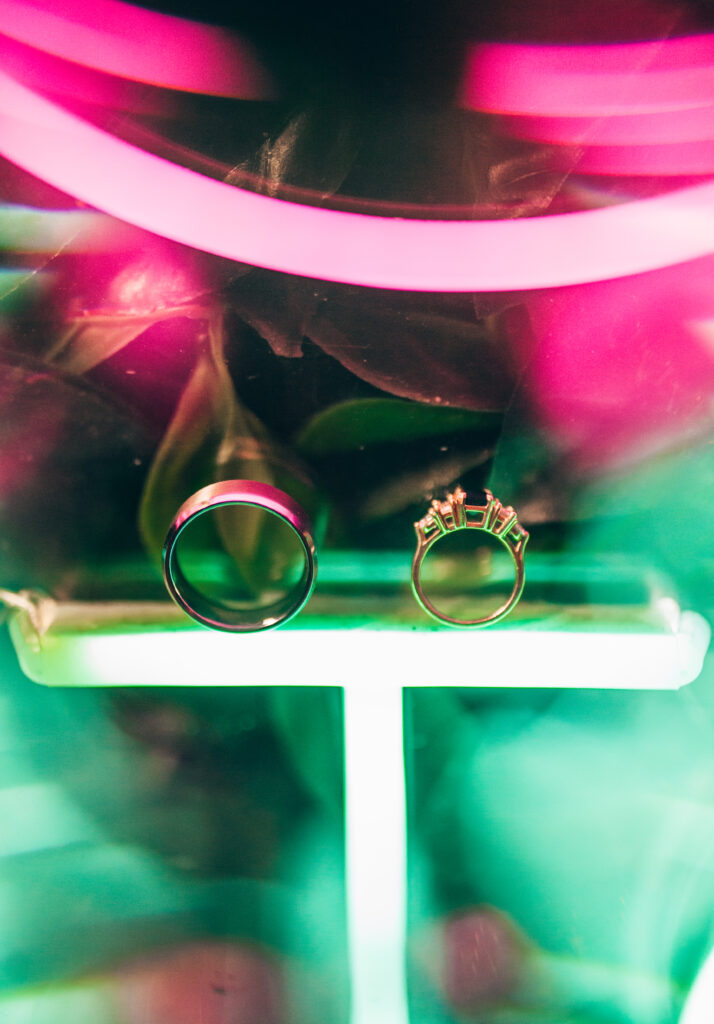 a man's wedding band and a woman's ring with a black center gem sitting upright on top of a neon light